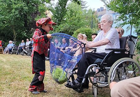 Ein Kinder-Clown interagiert mit einer Seniorin im Rollstuhl