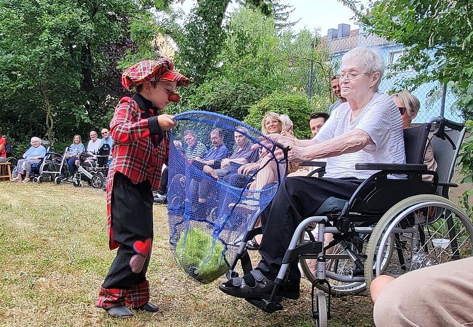 Ein Kinder-Clown interagiert mit einer Seniorin im Rollstuhl