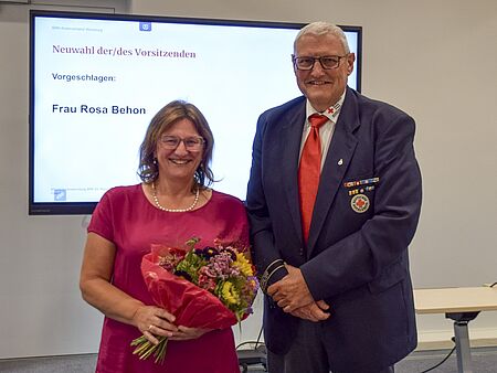 Eine Frau mit Blumenstrauß in der Hand und ein Mann in BRK-Anzug
