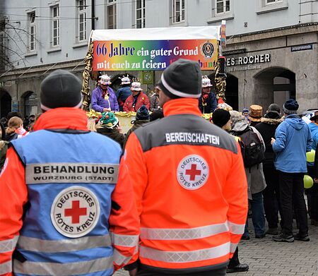 Zwei Sanitäter in BRK-Kleidung, mit dem Rücken zur Kamera, die den Faschingszug beobachten